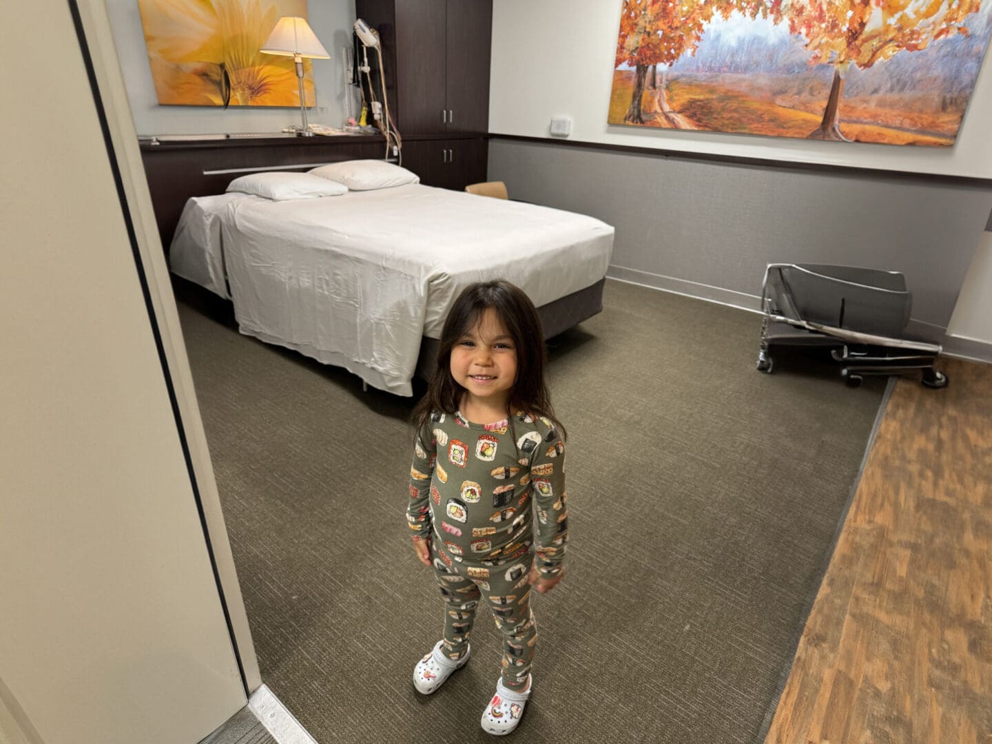 A little girl standing in front of a bed.