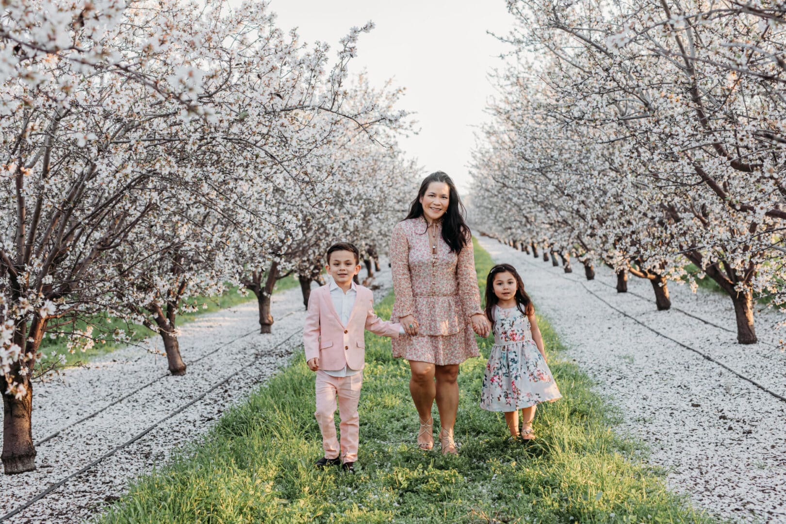 A woman and two children in the middle of an orchard.