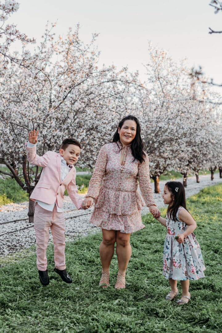 A woman and two children holding hands in front of trees.