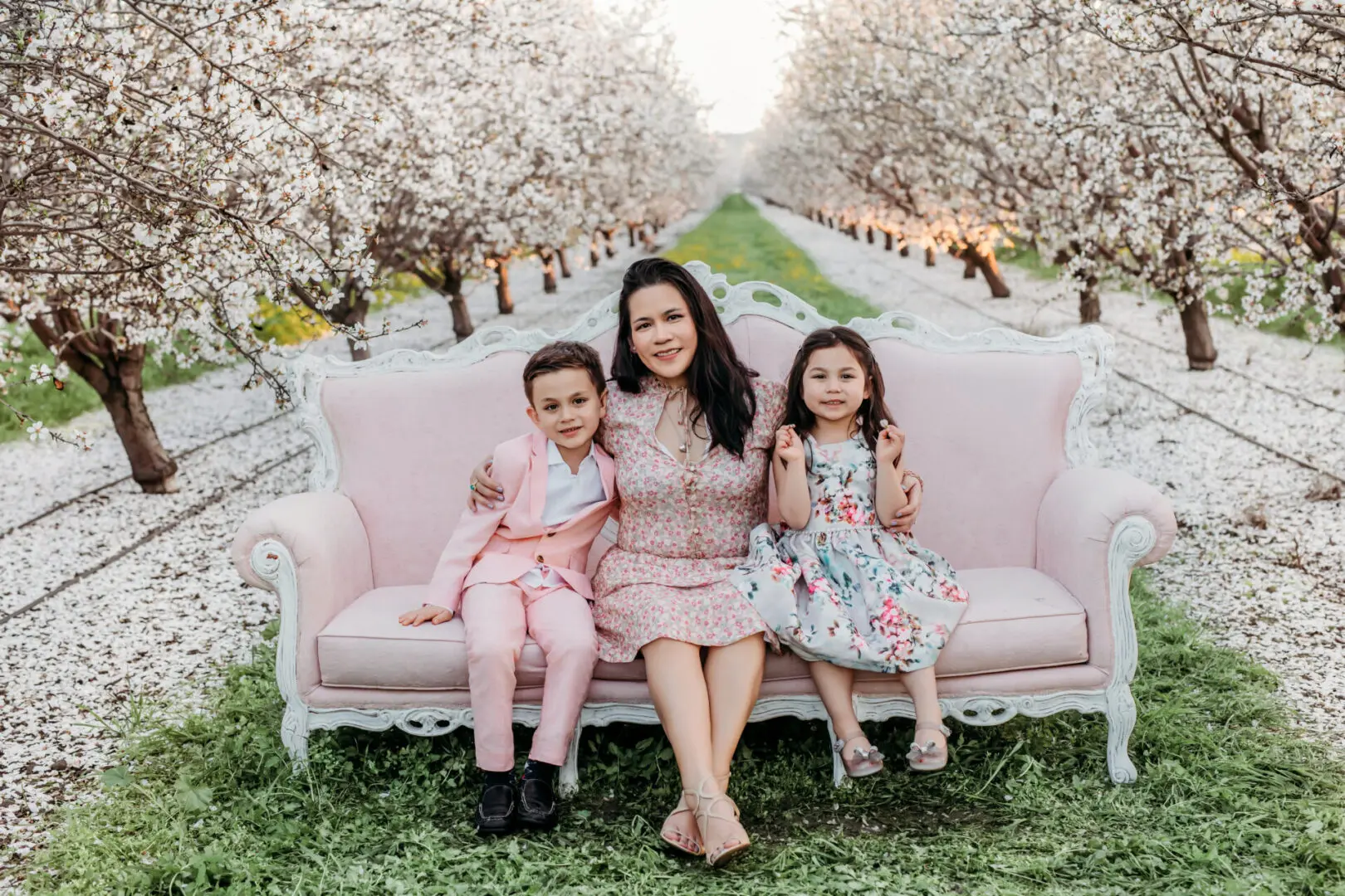 A woman sitting on top of a pink couch next to two children.