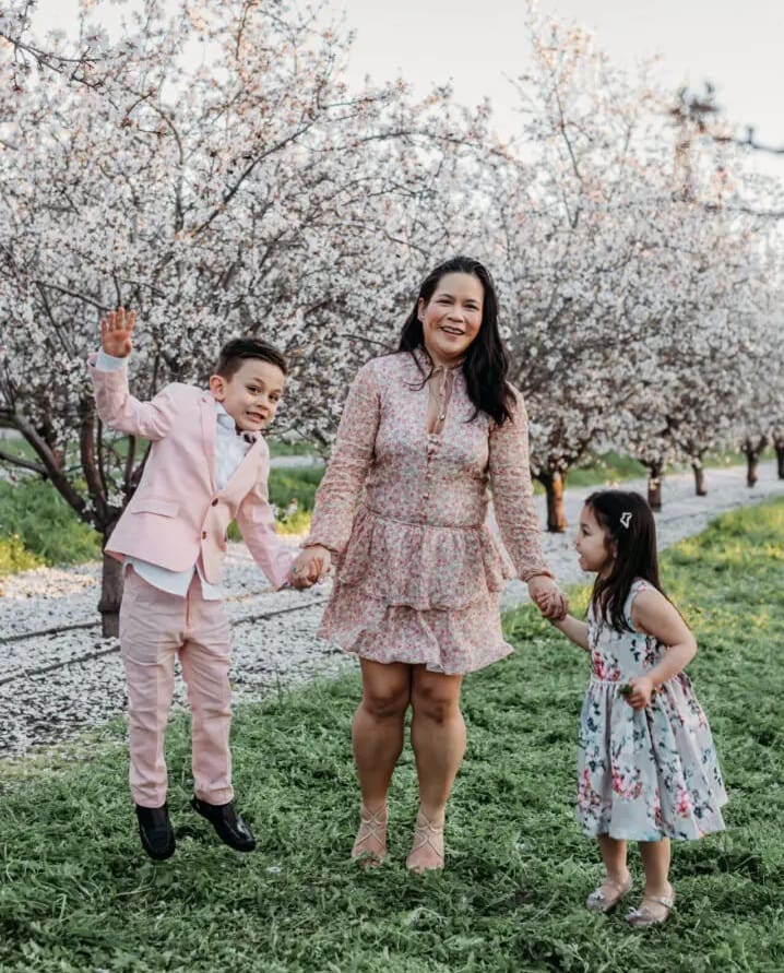 A woman and two children holding hands in front of an orchard.