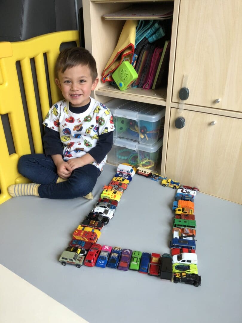 A boy sitting on the floor next to toy cars.