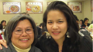 Two women smiling for a picture in front of some people.