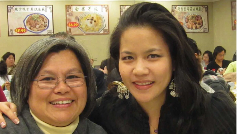 Two women smiling for a picture in front of some people.