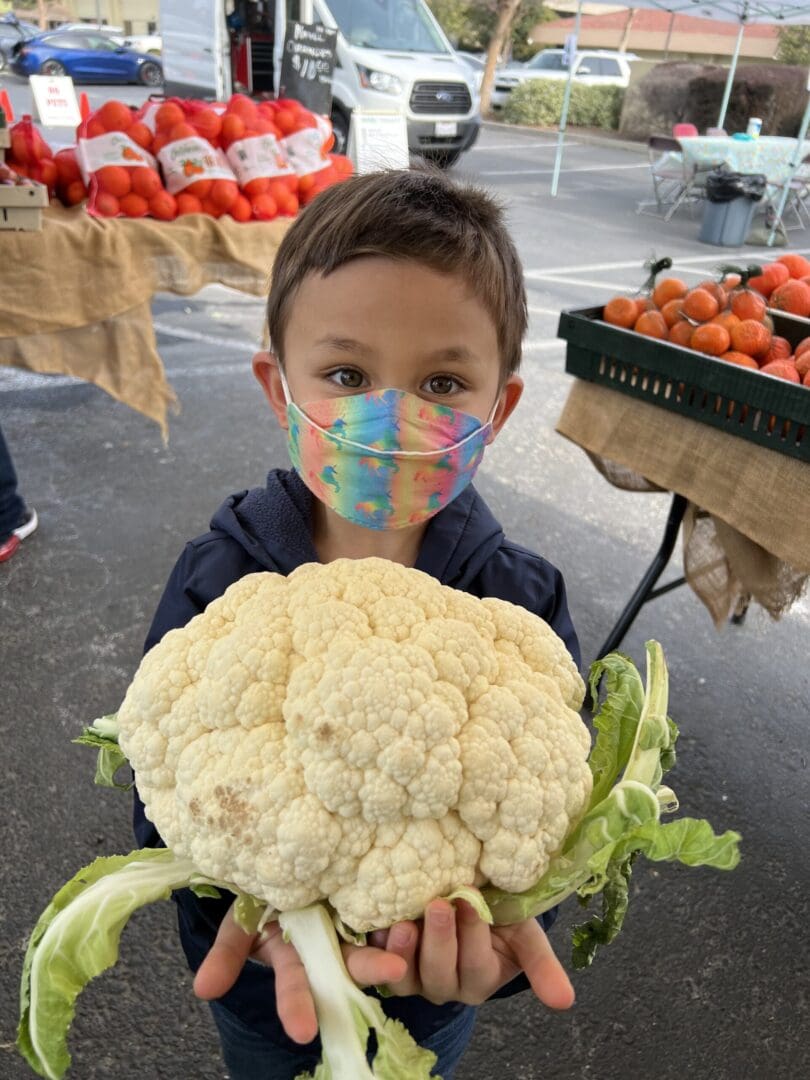 Child holding a giant cauliflower at market.