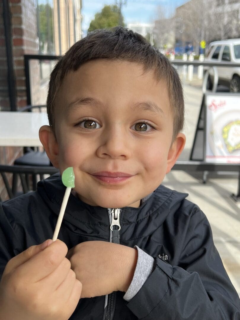 Smiling boy holding a green lollipop.