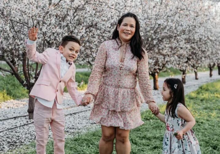 A woman and two children holding hands in front of an orchard.